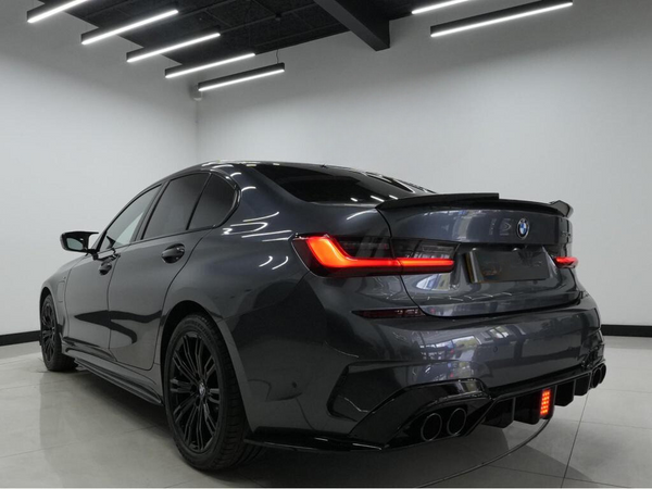 A dark gray car with tinted windows is parked in a well-lit room, showcasing sleek tail lights and a prominent rear bumper design.