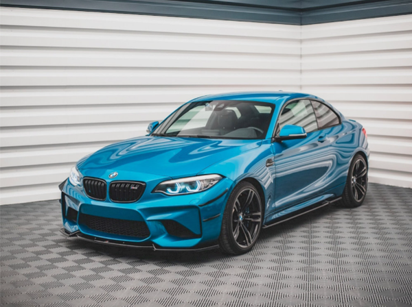 A blue sports car with a sleek, aerodynamic design is stationary on a patterned floor, surrounded by white paneled walls, creating a clean, showroom environment.