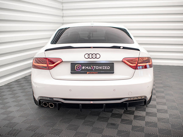 A white Audi car is stationary in a room with white, ribbed walls and checkered flooring. The rear license plate displays "#MAXTONIZED" with Instagram and Audi Sport logos.