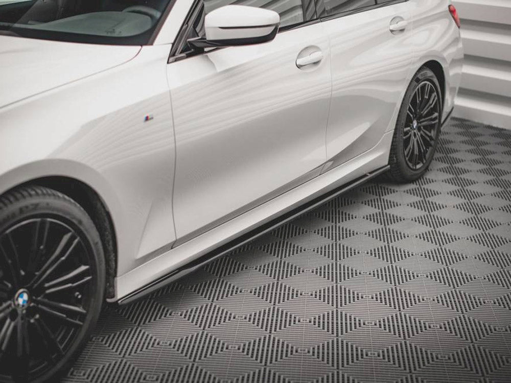 A white car with black alloy wheels is parked on a textured, patterned floor within a room with white walls.