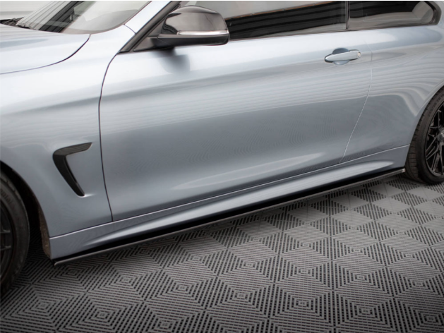 A silver car is parked on a patterned floor. The car's side features black trim and sleek, aerodynamic contours, with visible wheels and a closed door, reflecting a streamlined design.