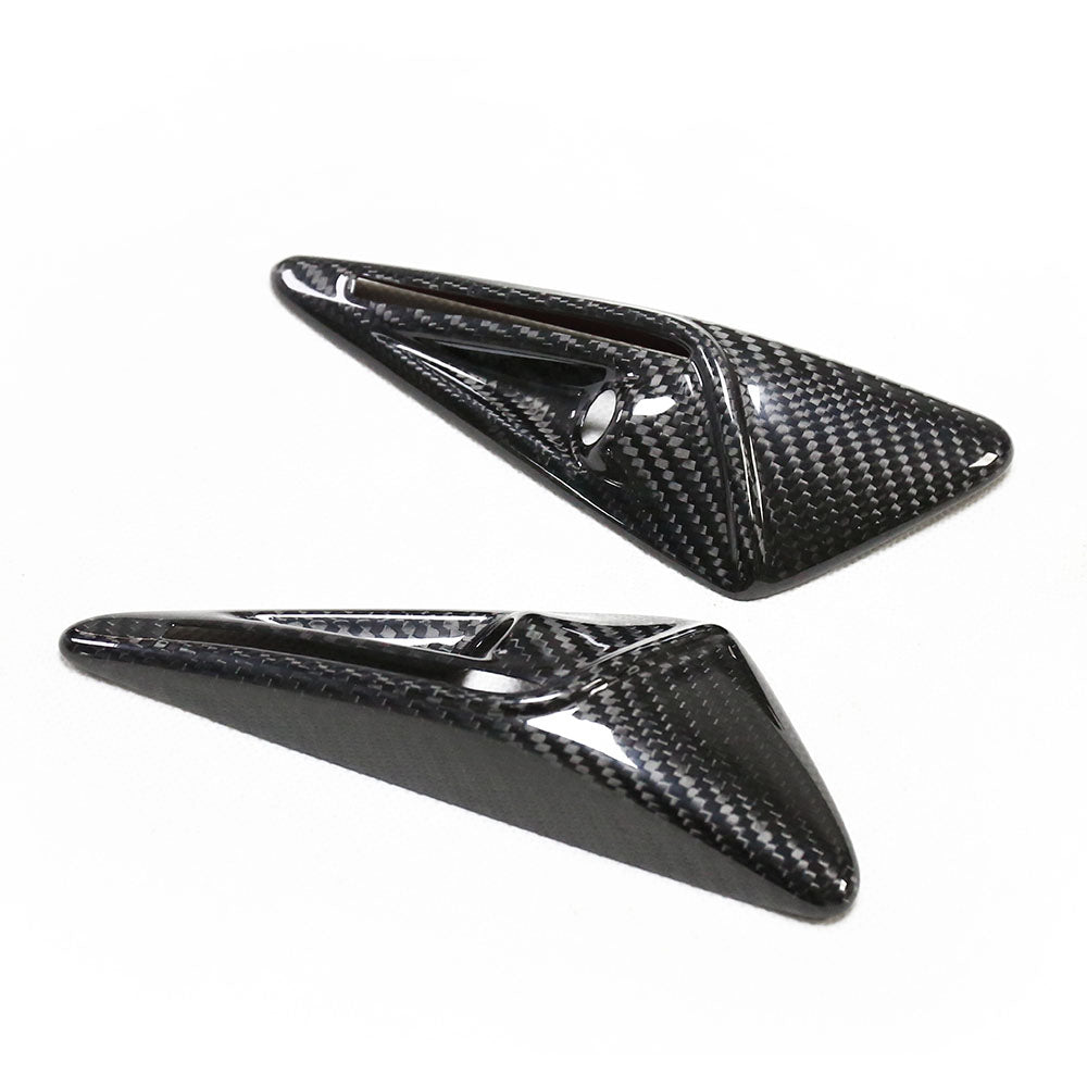 Two sleek, black carbon fiber triangular objects rest on a white surface, featuring glossy finishes with smooth, sharp edges and recessed grooves.