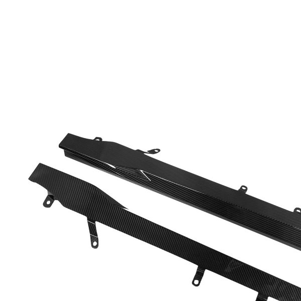 Two black carbon fiber car side skirts, angled with mounting brackets, lie on a white background. Their glossy surface reflects light, highlighting a sleek, textured pattern.