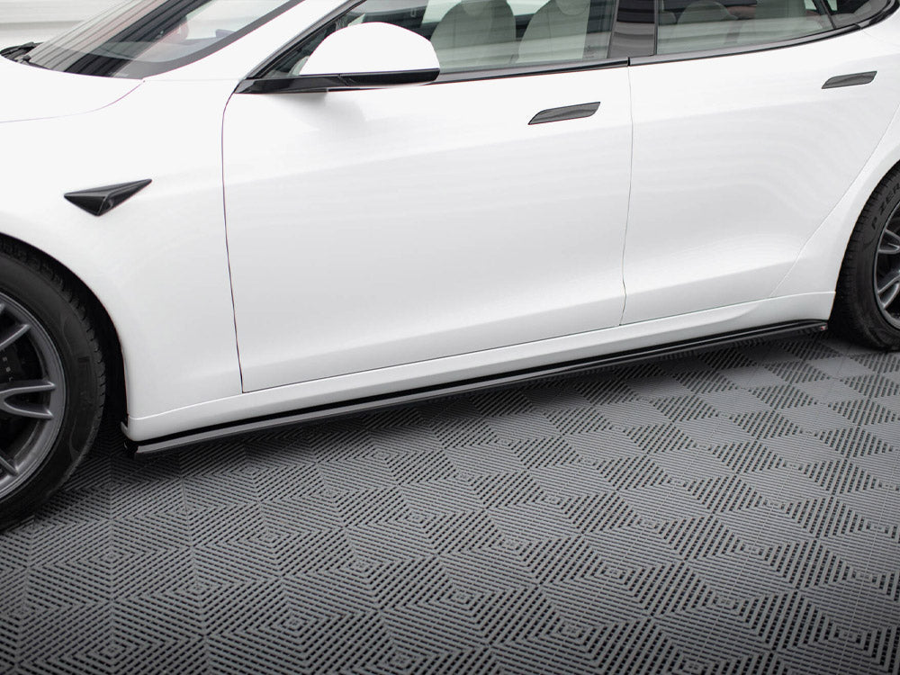 A white car is parked on a textured, geometric-patterned floor, showing its side profile with visible wheels and windows in a clean indoor setting.