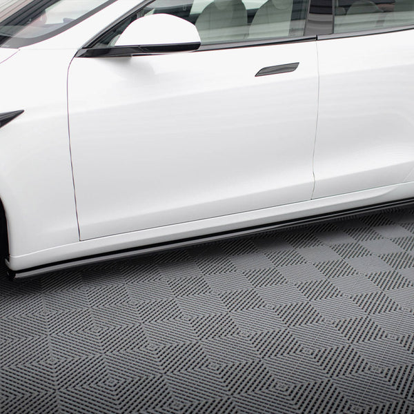 A white car is parked on a textured, geometric-patterned floor, showing its side profile with visible wheels and windows in a clean indoor setting.