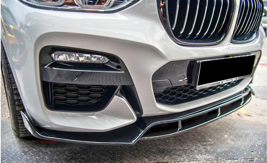 A car's front bumper with a grille and headlights sits on textured pavement. The bumper features honeycomb vents and sleek black accents, illustrating a sporty design.