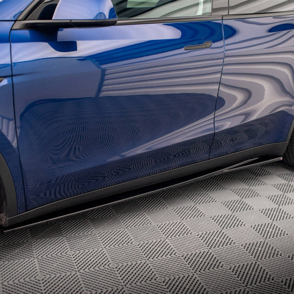 A blue car parked indoors with wavy patterns reflecting on its glossy surface, sitting on a textured, checkered floor. Black wheels and sleek design enhance its modern appearance.