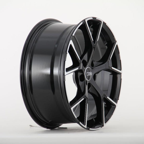 A black alloy wheel with a multi-spoke design and an Audi logo at the center is positioned upright against a plain, white background.