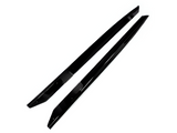 Two sleek, black, elongated plastic car side skirt extensions lie parallel on a white surface, appearing glossy and streamlined, designed for vehicle body modification.