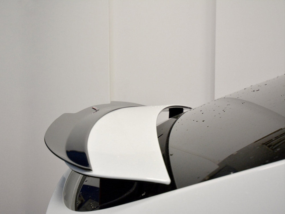 A white car's retractable spoiler is partially deployed, with water droplets on its surface, set against a plain indoor background.
