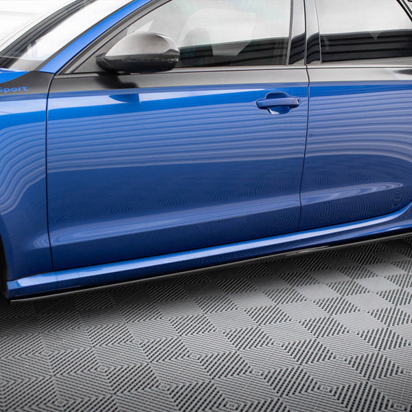 A blue car with "Audi Sport" text on the side stands on a checkered floor. The vehicle is viewed from the side, displaying its sleek design and black wheels.