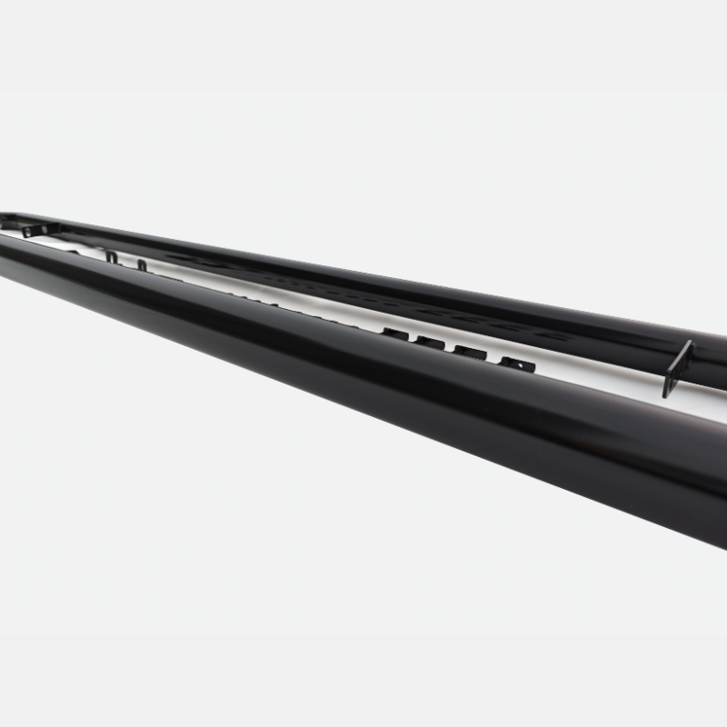 A long, black metal rail features a series of small protrusions along its surface, positioned against a plain white background, suggesting an industrial or architectural context.