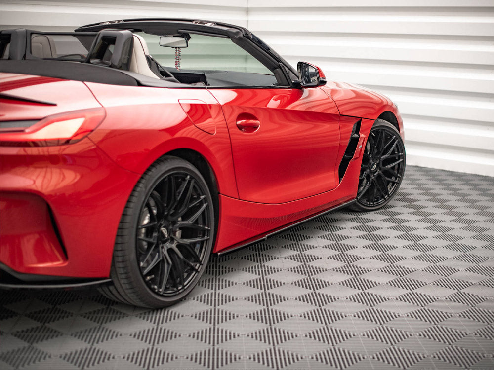 Red convertible sports car, parked, showcasing black wheels and sleek design. It sits on a patterned floor in a white-paneled garage.