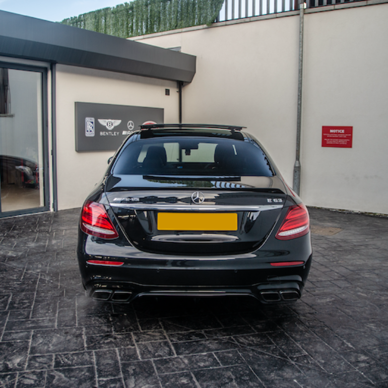 A black car is parked on a paved driveway outside a showroom with signs for Rolls Royce, Bentley, and Mercedes-Benz. A red notice reads, "NOTICE. PRIVATE PROPERTY. NO CUSTOMERS OR DELIVERY DRIVERS...".