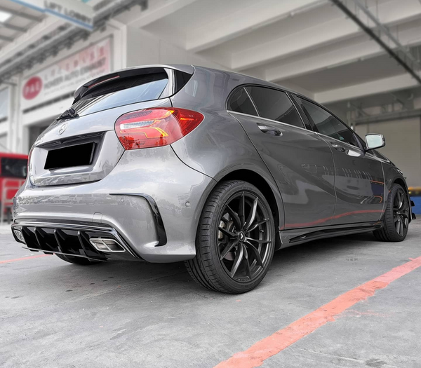 A silver hatchback is parked in a garage-like setting, emphasizing its rear design and black alloy wheels. Surrounding industrial structures create a modern, urban backdrop. No text is visible.