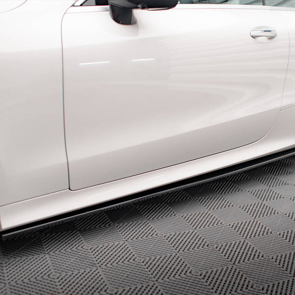 A white car parked on a patterned gray floor has visible side panels and wheels. The sleek design is highlighted by reflections on the clean surface.