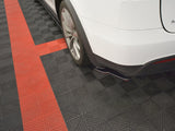 A white car's rear is parked on a checkered black and red garage floor. The car's tire is visible, and there are no visible markings or objects around.