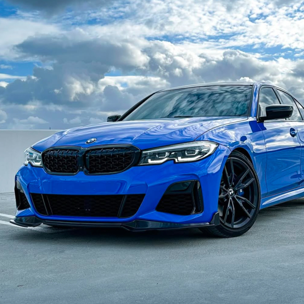 A blue BMW car is parked on a rooftop parking lot, under a cloudy sky with patches of blue.