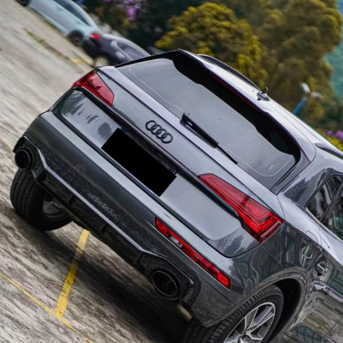 A gray Audi SUV parked on a sloped outdoor lot, surrounded by other vehicles. Trees and a distant mountain are visible in the blurred background, with no visible text.