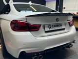 A white BMW 435d featuring a carbon fiber spoiler is parked inside a garage with a sign reading 