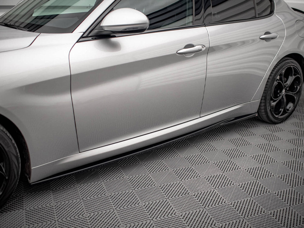 A silver car with sleek, aerodynamic design is parked on a textured, geometric-patterned floor. The car's side doors and black alloy wheels are visible, reflecting soft lighting.