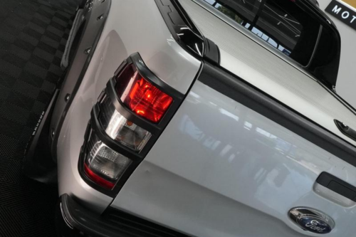 A white Ford pickup truck is parked on a black checkered floor, displaying its red and white taillights prominently. Reflections are visible on the vehicle's glossy surface.