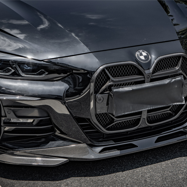 A black luxury car with a prominent grille and sleek headlights is parked on a road. Sunlight reflects off its shiny surface, highlighting its modern design. The BMW logo is visible.