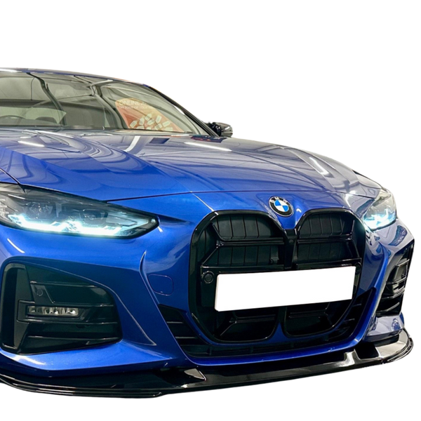 A blue BMW with illuminated headlights is parked indoors, displaying a large black grille and blank license plate, reflecting ceiling lights on its polished surface.