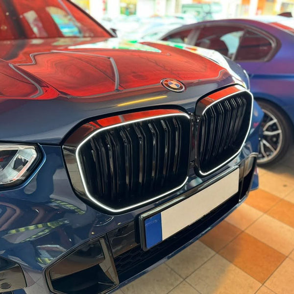 A shiny blue car features a prominent front grille and logo, parked next to another blue car in an indoor showroom with a tiled floor and overhead lighting.