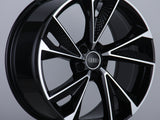 A glossy, black alloy wheel features silver accents and the Audi logo at the center, displayed on a neutral gray background with a studio setting.