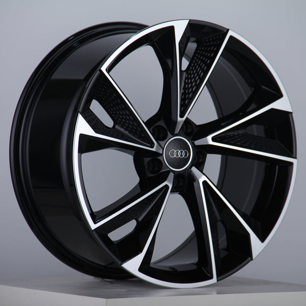 A glossy, black alloy wheel features silver accents and the Audi logo at the center, displayed on a neutral gray background with a studio setting.