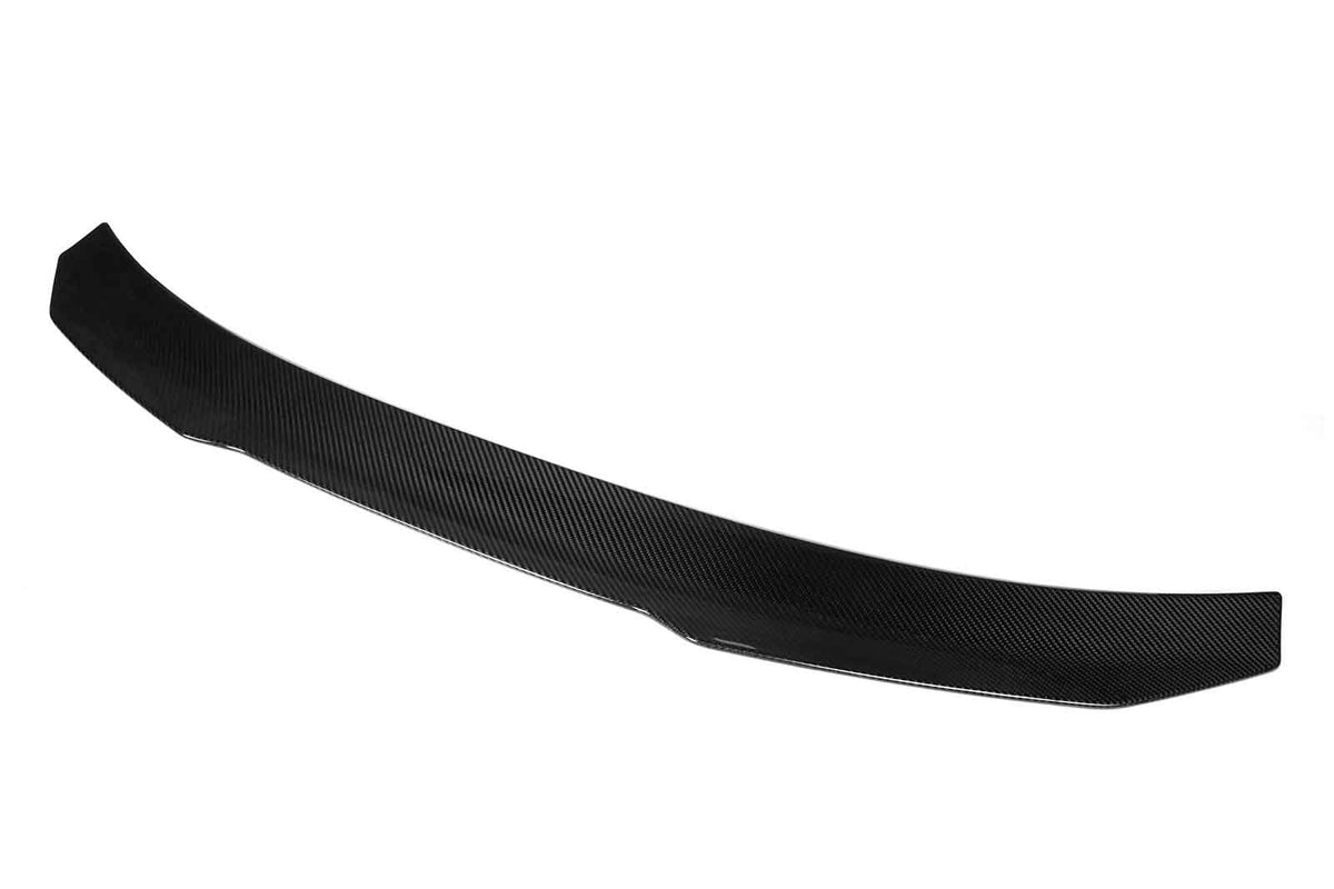 A carbon fiber car spoiler with a sleek, curved design rests against a plain white background, highlighting its aerodynamic structure and lightweight material.