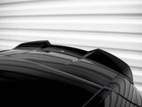 A shiny black car roof features an aerodynamic fin. It's positioned against a blurred, horizontally-striped, white background, creating a sleek and modern appearance.