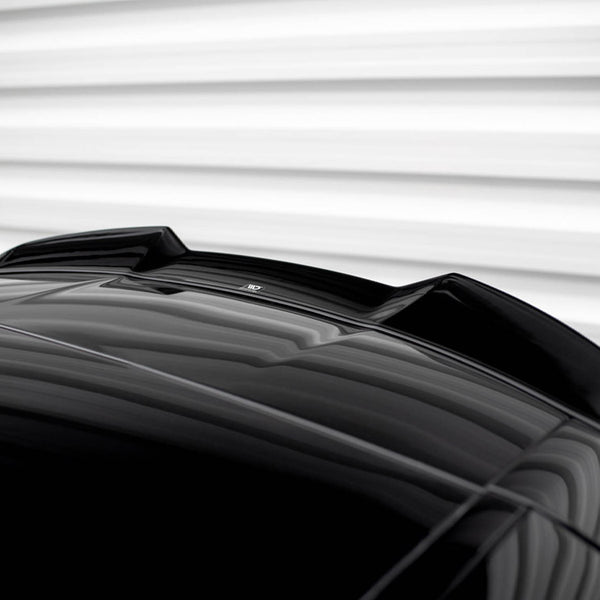 A shiny black car roof features an aerodynamic fin. It's positioned against a blurred, horizontally-striped, white background, creating a sleek and modern appearance.
