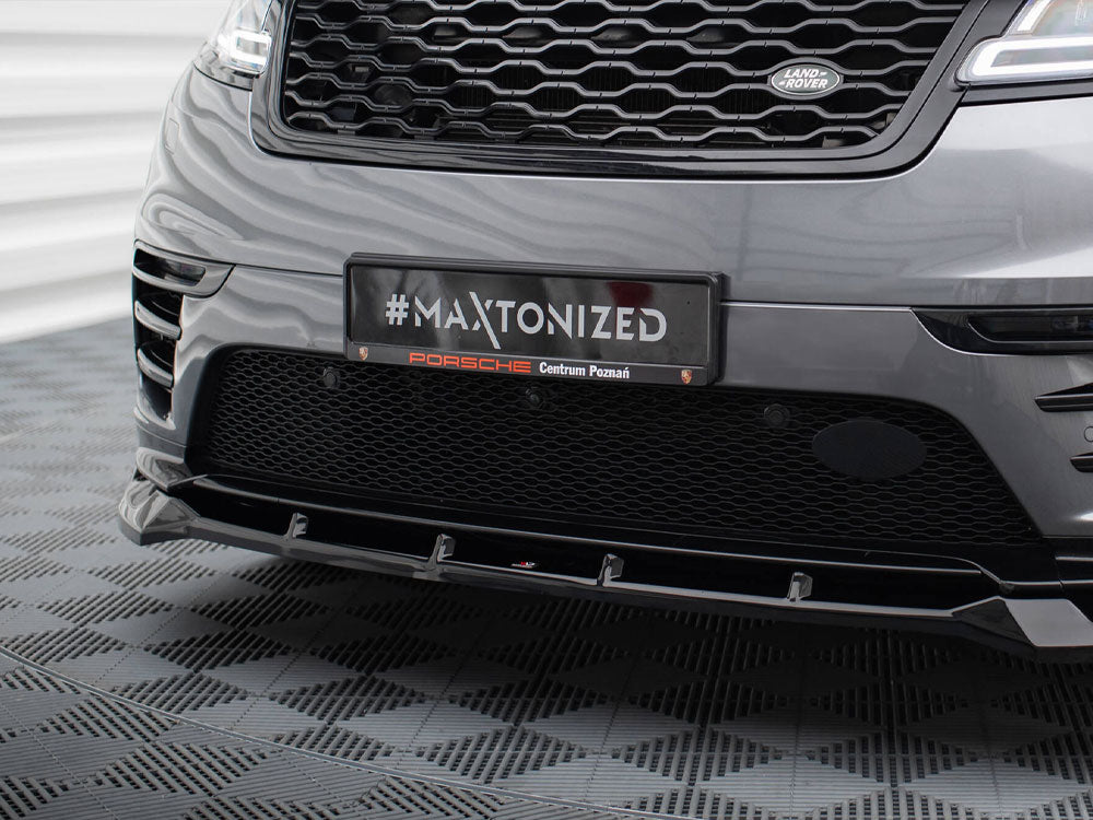 A car's front bumper with a grille displays a plaque reading "#MAXTONIZED Porsche Centrum Poznań" in a patterned indoor setting.