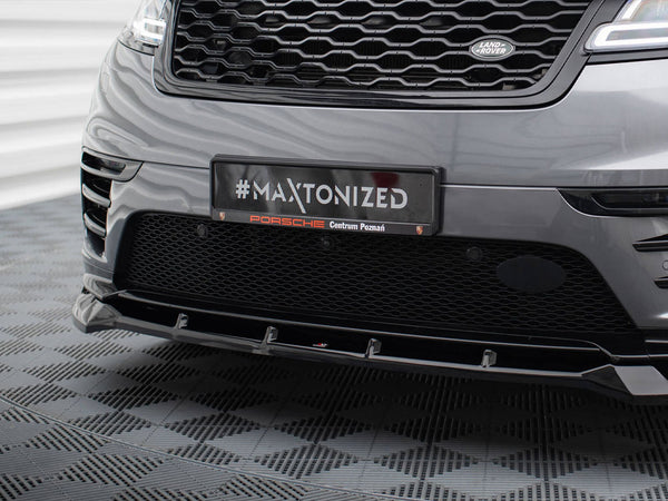 A car's front bumper with a grille displays a plaque reading "#MAXTONIZED Porsche Centrum Poznań" in a patterned indoor setting.