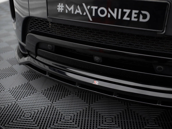 A black car's front bumper displays the text "#MAXTONIZED" on a license plate with a hexagonal grille, parked on a patterned rubber mat.
