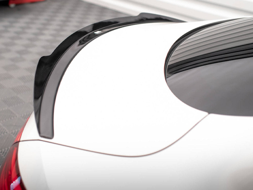 A sleek black spoiler rests on the rear of a white car, positioned in an indoor space with a checkered floor, adjacent to red car components.