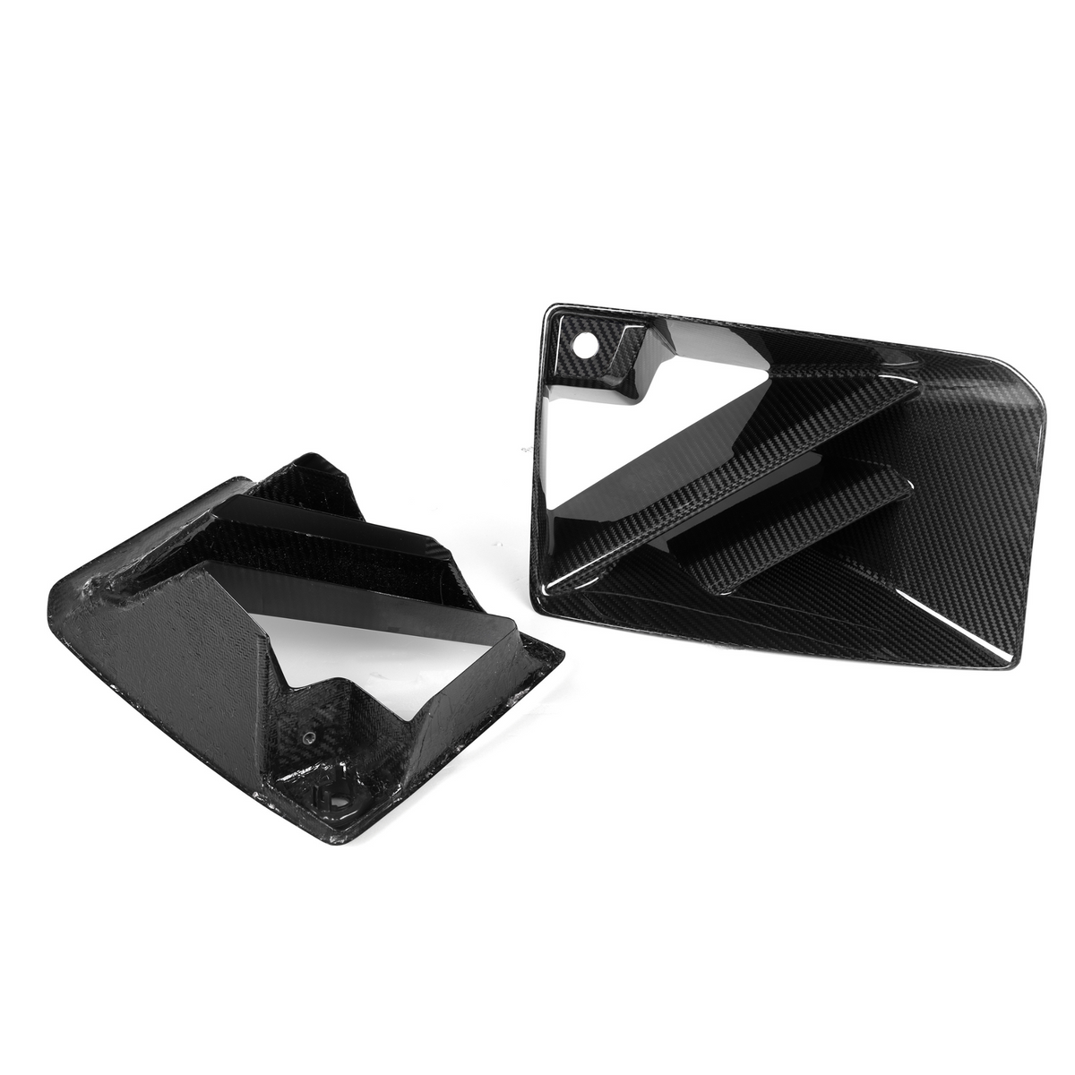 Two black, angular carbon fiber car parts are positioned on a white background. One lies flat, showing its patterned surface, while the other stands upright, revealing defined geometric angles.