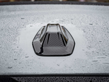 A black, shark fin car antenna rests on a gray, wet car roof, with raindrops scattered across the surface creating a textured appearance.