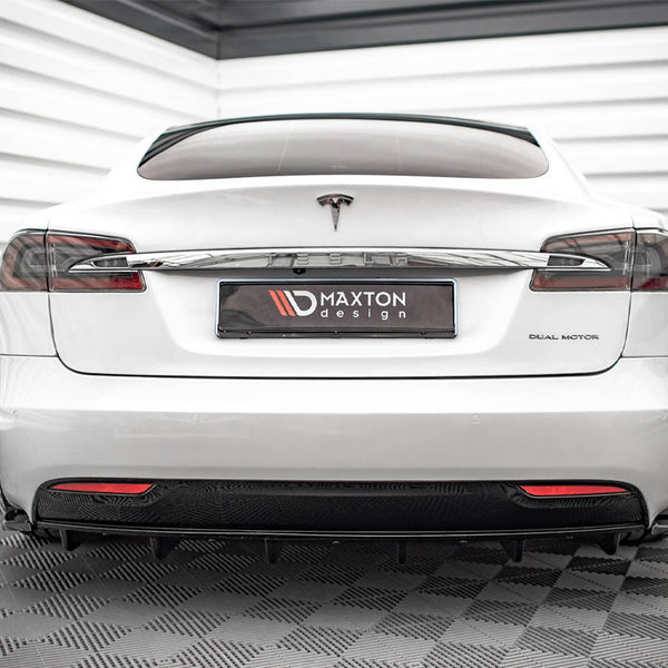 A white Tesla car is parked indoors on a textured floor, with "DUAL MOTOR" on the right and a "MAXTON design" plate in the center.