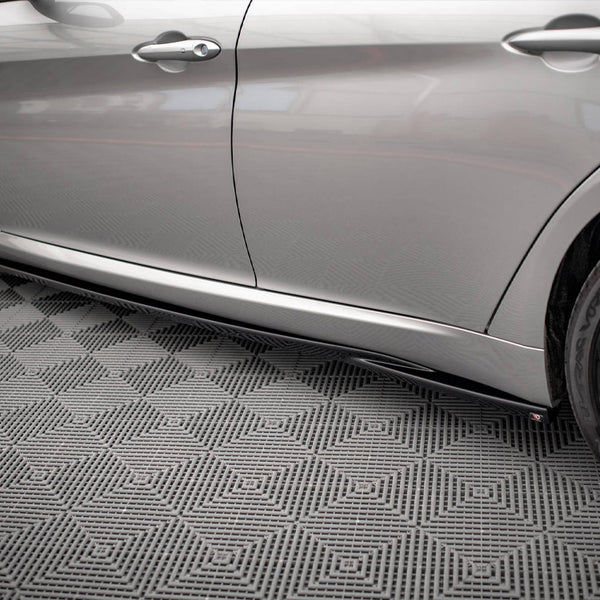 A silver car with black wheels is parked on a patterned, interlocking gray floor. The side profile emphasizes its sleek design and closed doors, with no text visible.
