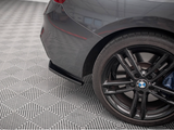 The image shows the rear wheel and bumper of a gray BMW car, parked on a patterned floor in an indoor space.