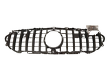 A black car grille with a central circular opening is laid on a plain white background. A small plastic bag containing screws is near the right side of the grille.