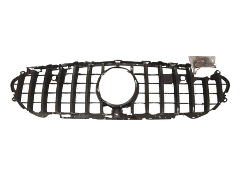A black car grille with a central circular opening is laid on a plain white background. A small plastic bag containing screws is near the right side of the grille.