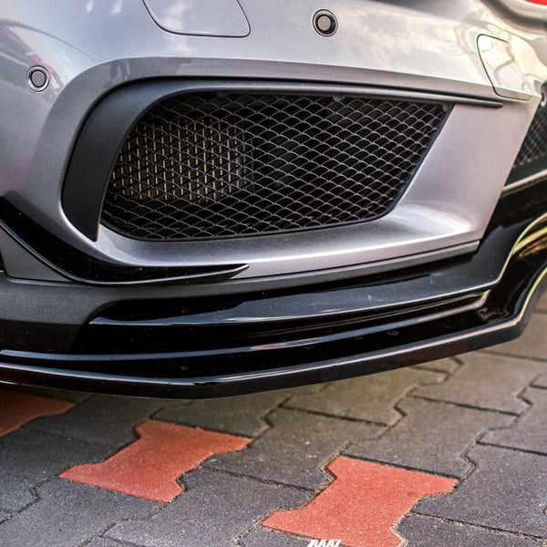 A grey car's front bumper with a black splitter and mesh grille is parked on a red and gray tiled surface.
