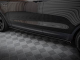 A black car rests on a geometric-patterned floor, reflecting striped wall patterns across its shiny side surface in an enclosed environment.