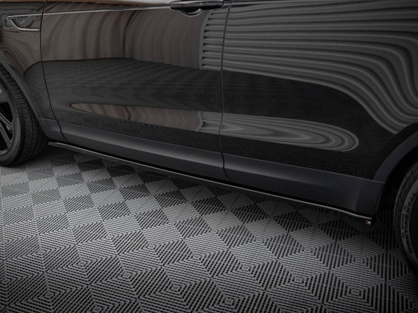 A black car rests on a geometric-patterned floor, reflecting striped wall patterns across its shiny side surface in an enclosed environment.
