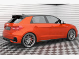 A bright orange hatchback car is parked on a checkered floor in a well-lit garage. The car features alloy wheels and a license plate reading 