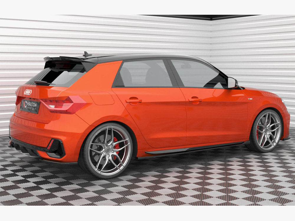 A bright orange hatchback car is parked on a checkered floor in a well-lit garage. The car features alloy wheels and a license plate reading "Maxton Design."